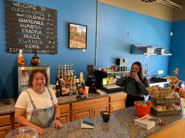 Sheri Knight, owner and her employee behind the coffee bar. Her employee is drinking from a coffee mug. The walls are blue and there's a menu written in chalk. 