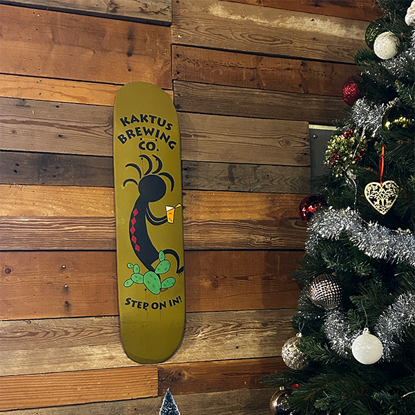 A skateboard with Kaktus Brewing's logo is mounted on their wood plank walls next to a Christmas tree.